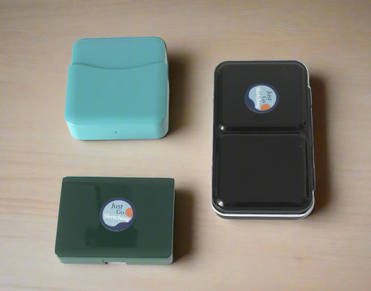 Three rectangular containers with lids, two in teal and one in black, on a white background.